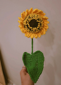 Handmade yellow crochet sunflower with green leaf on stem.