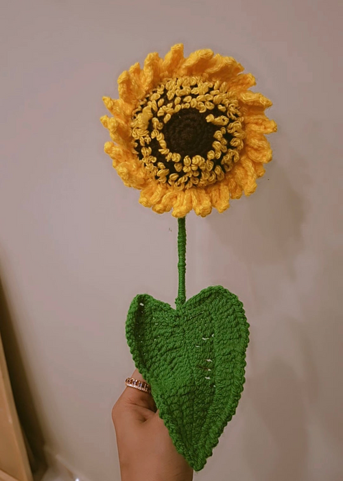 Handmade yellow crochet sunflower with green leaf on stem.